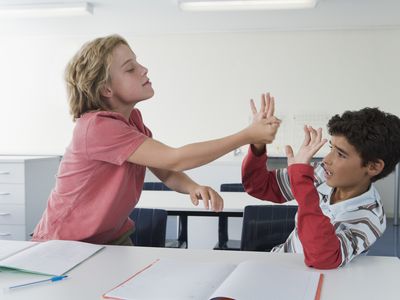 School boys (10-13) in classroom fighting, one boy hitting the other, bullying