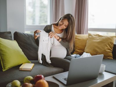 An expecting mom showing a baby outfit to her computer during a virtual baby shower