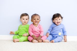 三个穿着绿色，粉色和蓝色衣服的婴儿。