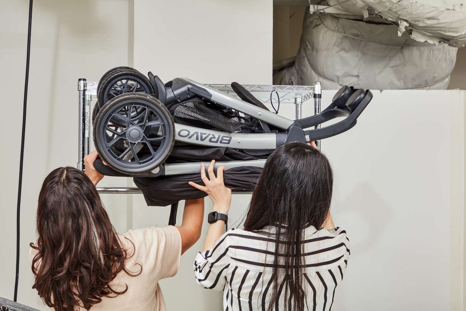 Two women taking out the folded Chicco Bravo Trio Travel System from the rack