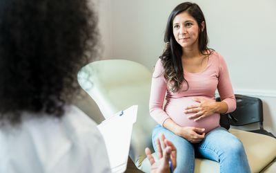 孕妇在听医生讲课时抚摸腹部。医生一边拿着病人的病历，一边做手势。