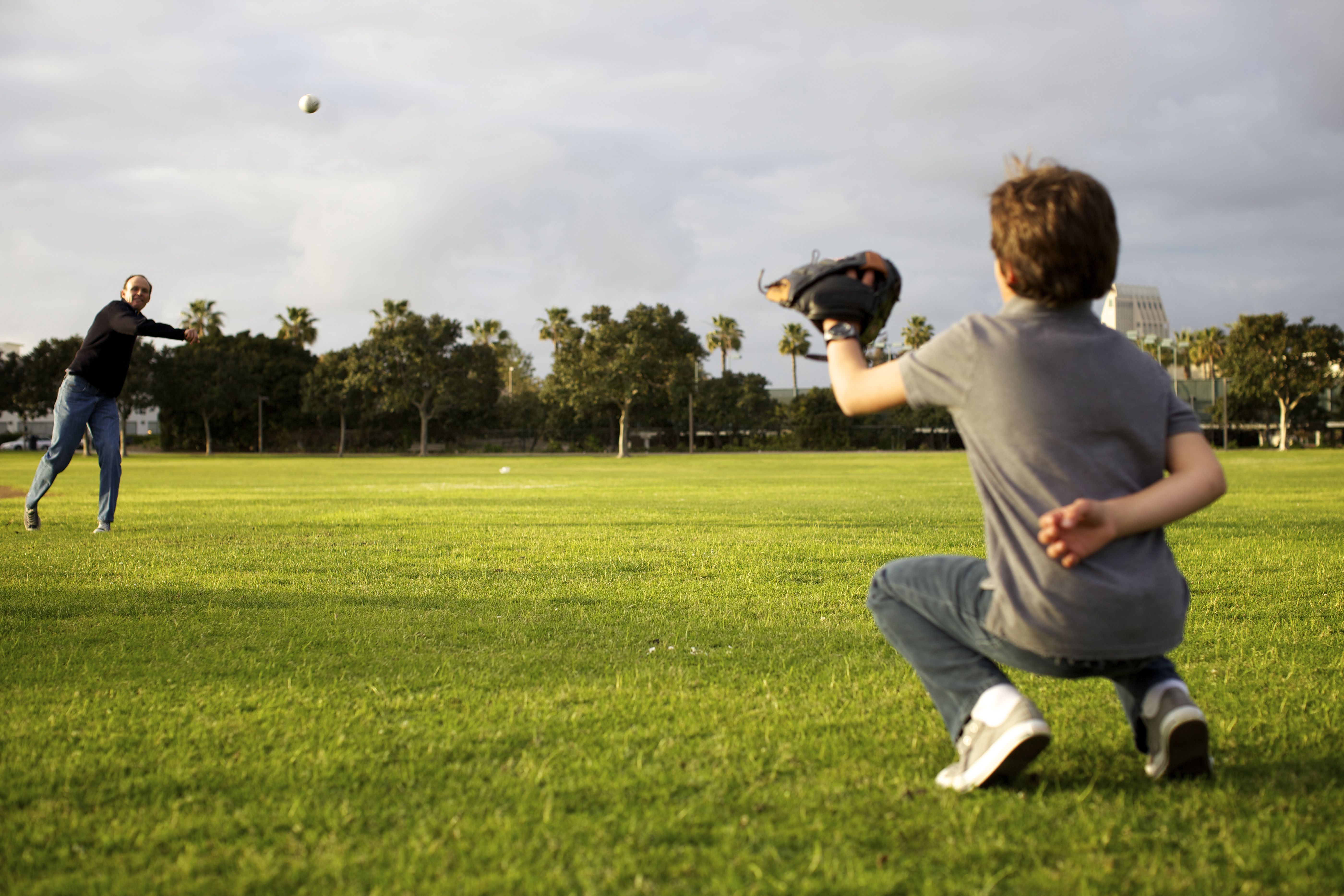 A grandfather throws a baseball to his grandson in a park