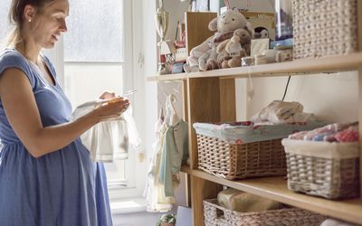 A pregnant woman in a nursery sorting out baby clothes.