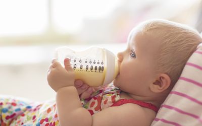 Baby girl drinking from bottle on sofa