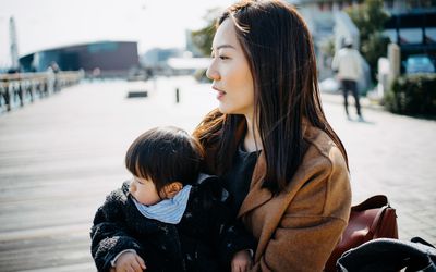 年轻的亚洲单身母亲抱着可爱的小女儿坐在码头边沉思