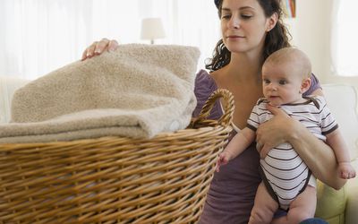 Woman folding laundry while holding a baby
