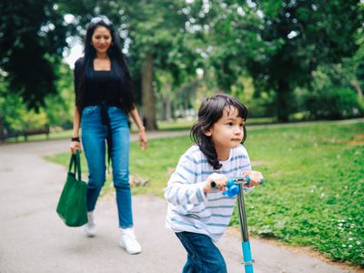 toddler on scooter while mom watches at park.