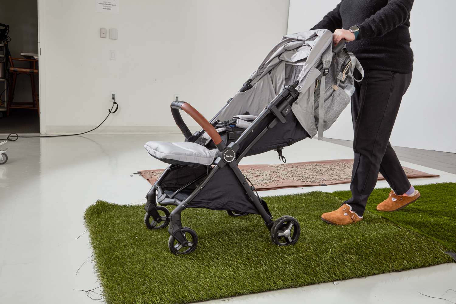A person pushes a Silver Cross Jet 3 Super Compact Stroller on fake grass