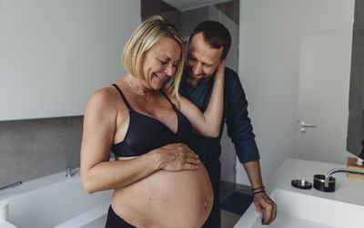 快乐的成熟孕妇夫妇在浴室看着准妈妈的肚子