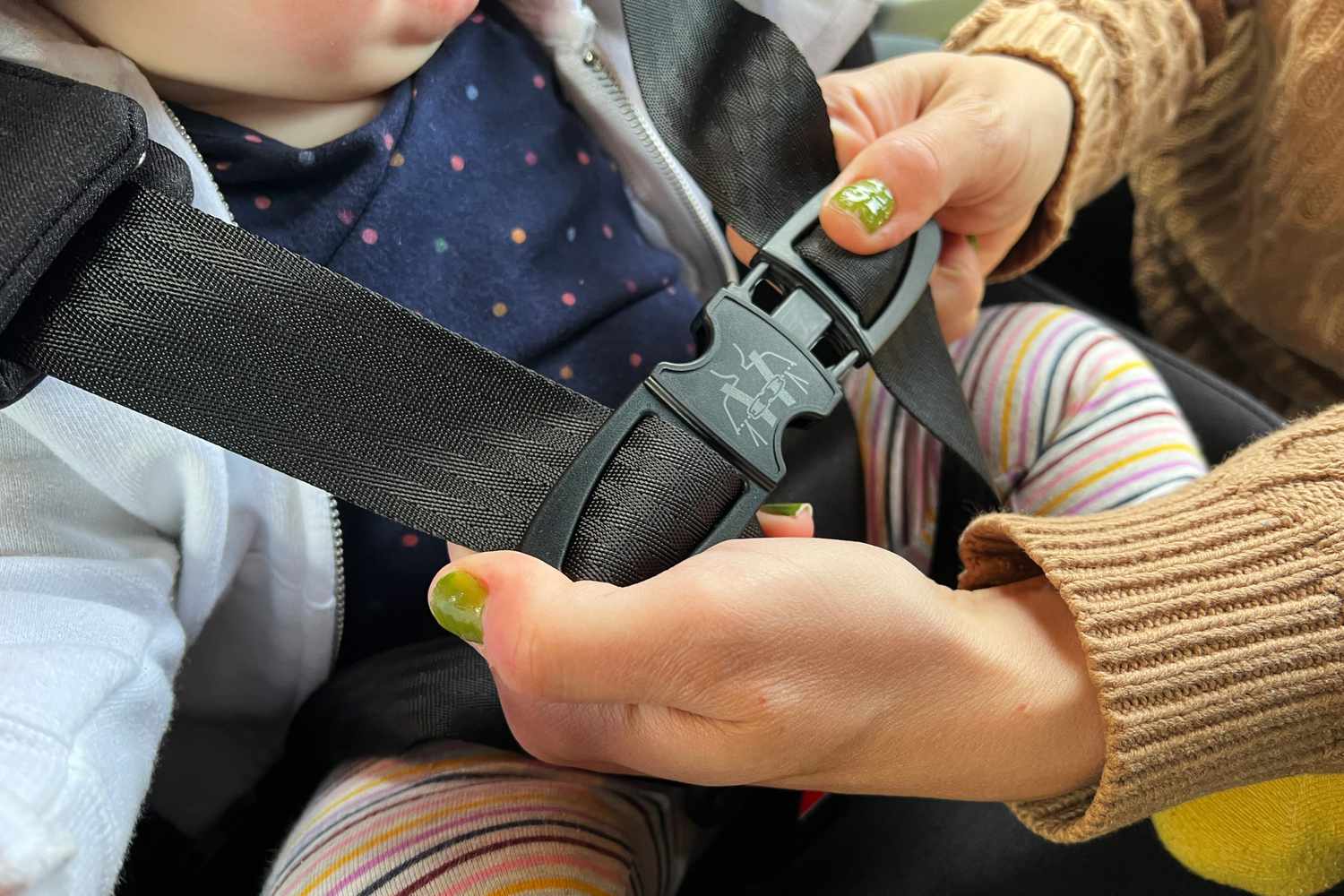 Person securing their child in the Clek Foonf car seat