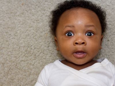 adorable baby with big eyes laying on a rug