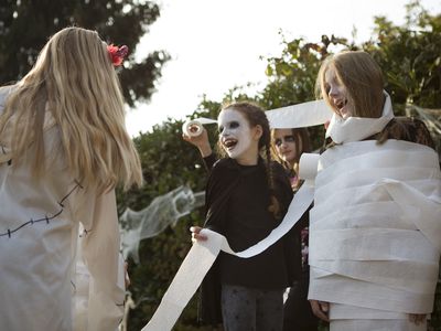 Group of older children playing 'wrap the mummy' Halloween game with toilet rolls