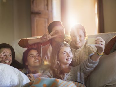 Group of smiling teenagers taking selfie on sofa in living room