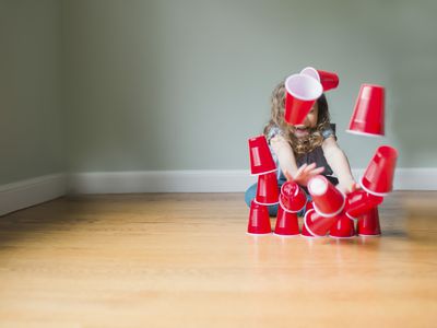Playful girl breaking pyramid made of disposable cups while sitting on floor at home