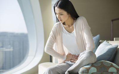 年轻女子抱着疼痛的腹部在沙发上