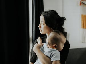 一位年轻的母亲望着窗外的阳光，怀里抱着她的婴儿