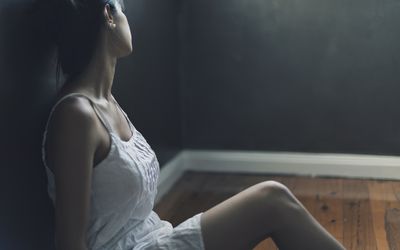 沮丧的女人坐在地板上，靠在墙上