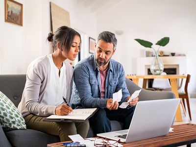 couple calculating bills at home using laptop and calculator.