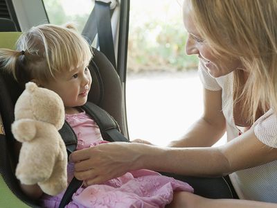 Mother fastening little girl into car seat