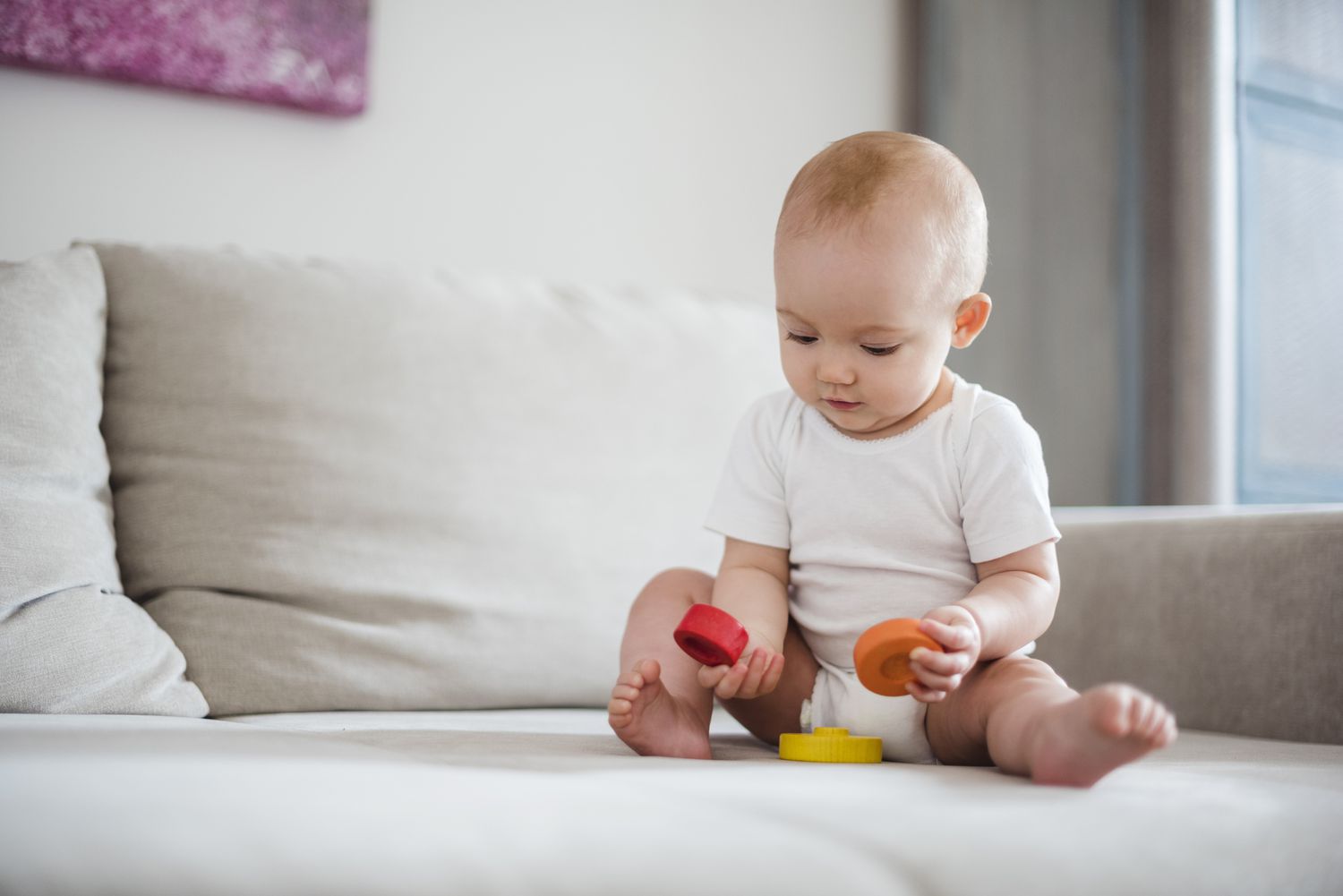 baby sitting on a couch playing with round blocks