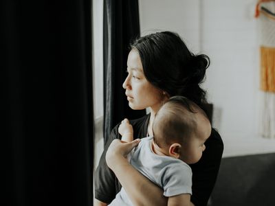 一位年轻的母亲望着窗外的阳光，怀里抱着她的婴儿