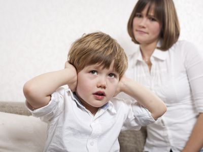 defiant young boy covering his ears while annoyed mother looks on