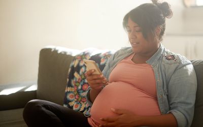 一名孕妇坐在家里的客厅里发短信