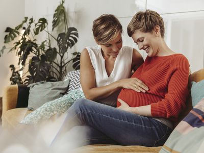 Pregnant surrogate and intended mother touching belly of the expectant mother