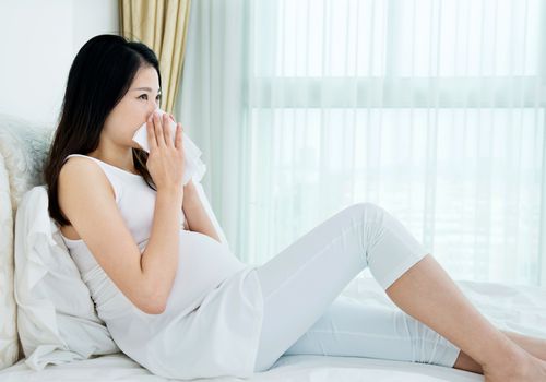 孕妇坐在床上用纸巾擤鼻涕
