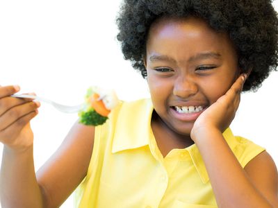 young girl making face eating vegetables