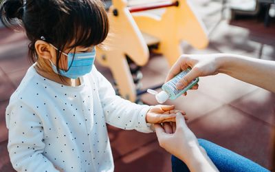mom putting hand sanitizer in the hand of asian child in mask