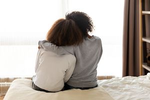 Rear view of mother and daughter sitting on bed