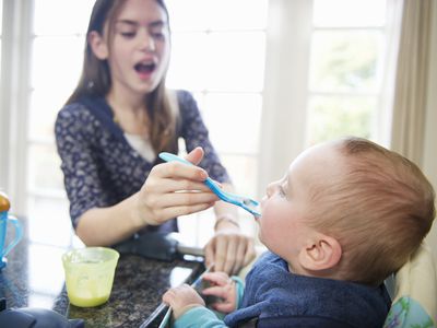 A young woman feeding a baby in a high chair