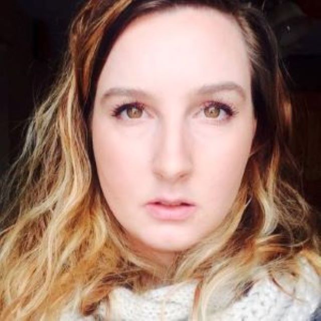 劳伦看着相机和穿ing a tan scarf. Lauren has brown eyes, white skin, and wavy brown hair.
