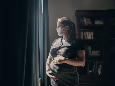 一位戴着口罩的孕妇望向窗外