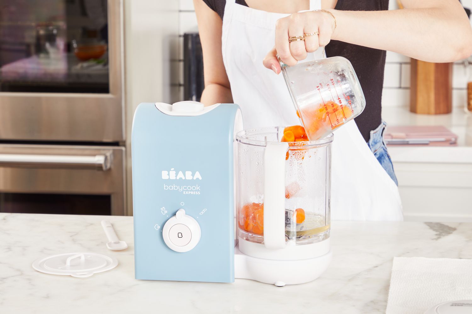 A person pours a cup of carrots into the BÃ©aba Babycook Express Baby Food Maker.