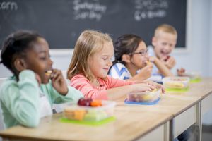 elementary age children are sitting at their desks and are eating their healthy snacks