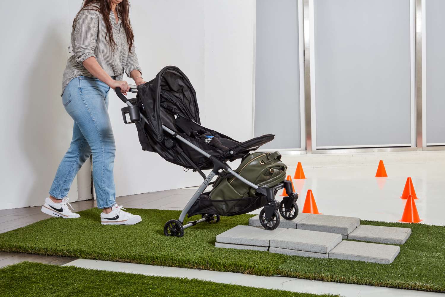 Person pushing Safety 1st Teeny Ultra Compact Stroller on stone floor above fake grass