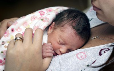 “新生的早产女婴，才出生两天，躺在妈妈的乳房上。”