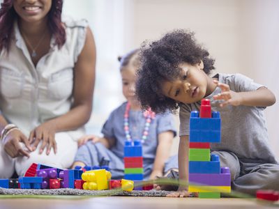 toddler boy playing with building blocks while mom and sister watch