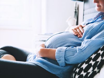 pregnant woman sitting at bed and holds hands on belly in bedroom at home.