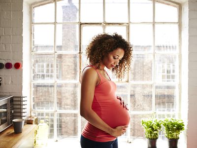 A pregnant woman standing in a kitchen holding her stomach
