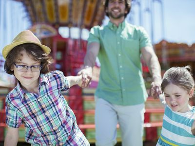 Girl and boy pulling their father in amusement park