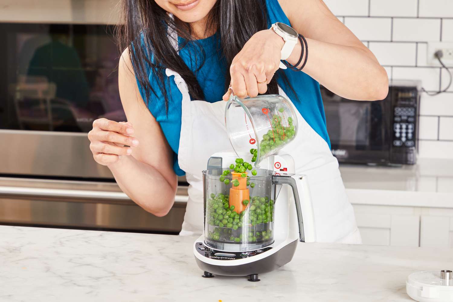 A person pours peas into the Baby Brezza One Step Glass Baby Food Maker.