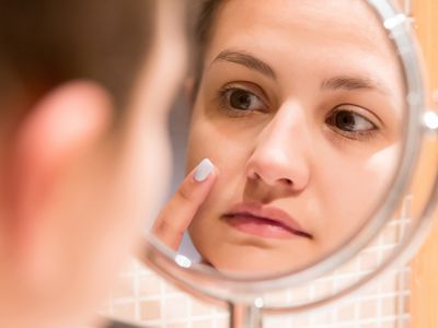 Woman looking into a close-up mirror, examining her skin.