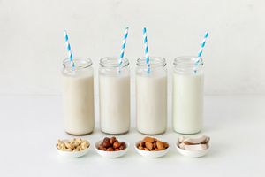 A vignette of four jars with non-dairy milk have blue and white striped straws.