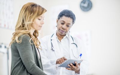 woman and female doctor looking at tablet in office