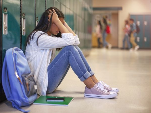 Side view of high school girl in illuminated corridor. She is against metallic lockers.