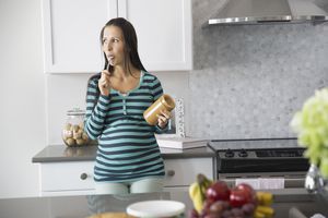 Pregnant woman eating peanut butter in kitchen