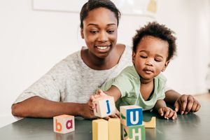 Person holding a child on their lap while they stack wooden alphabet blocks on a hard surface